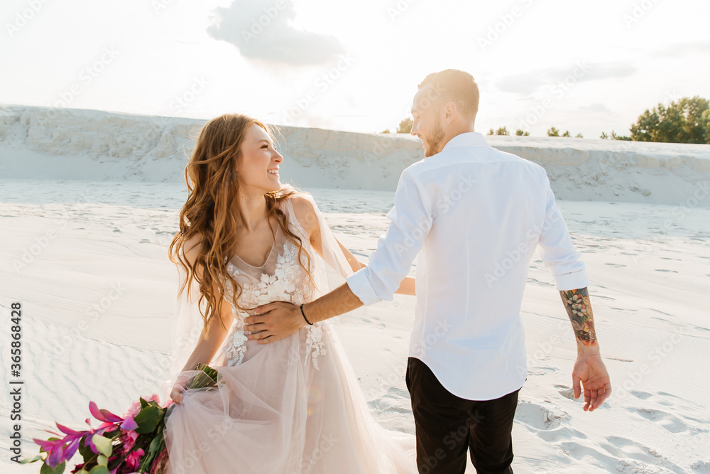 Love Story of a beautiful couple in a pink wedding luxury dress with a bouquet in the Sahara desert, sand, dunes Love Story of a beautiful couple in a pink wedding luxury dress with a bouquet in the Sahara desert, sand, dunes