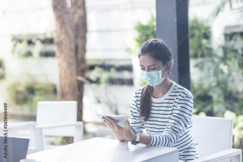 Asian young businesswoman in casual wear wearing medical face mask working with the tablet while sitting outside the office. Social distancing. Asian young businesswoman in casual wear wearing medical face mask working with the tablet while sitting outside the office. Social distancing.