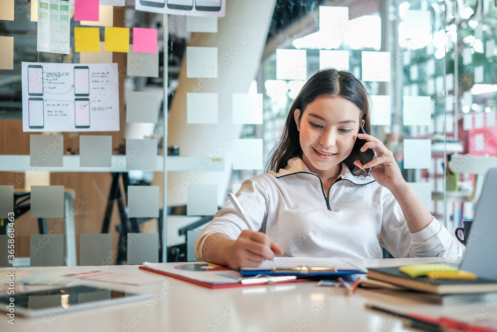 Beautiful asian woman is cheerful, talking on a mobile phone and using a laptop and smiling happily while working. Beautiful asian woman is cheerful, talking on a mobile phone and using a laptop and smiling happily while working.