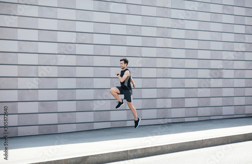 Jogging with jumping. Guy runs at path near gray brick wall in city