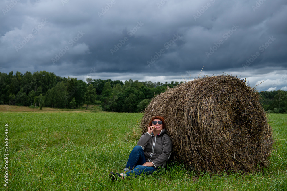 woman resting near a haystack in nature against a gray sky woman resting near a haystack in nature against a gray sky