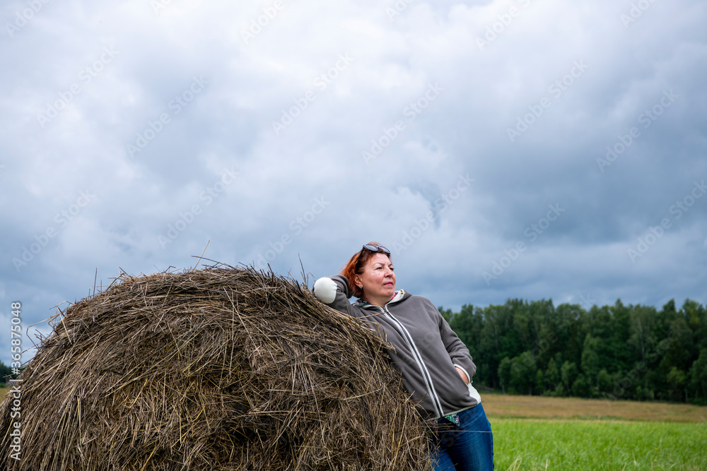 woman resting near a haystack in nature against a gray sky woman resting near a haystack in nature against a gray sky