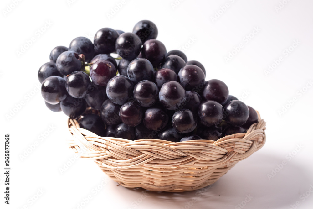 Black grapes without seeds in a rattan basket. White background Black grapes without seeds in a rattan basket. White background