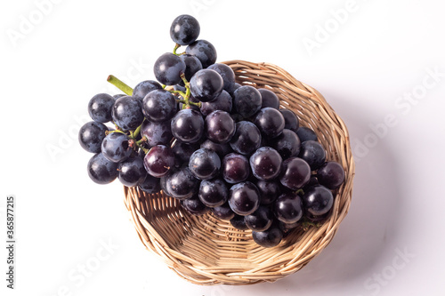 Black grapes without seeds in a rattan basket. White background