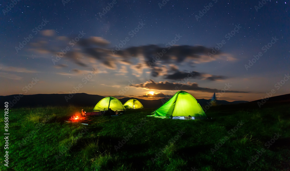 Camping in mountains at night. Colorful sunset with dramatic sky.  illuminated tents in mountains. Travel recreational outdoor activity concept. Carpathian mountains. Ukraine.