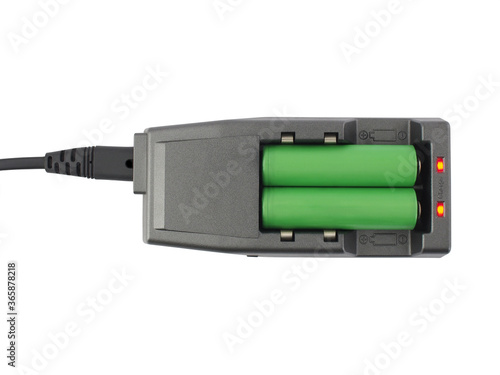 two green rechargeable batteries are charging in dark gray battery charger with red indicator light isolated on white background, flat lay close up top view