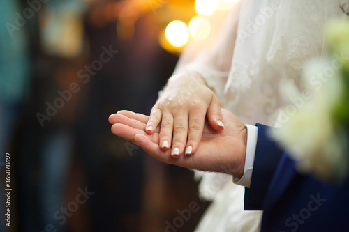 Hands of the newlyweds at the wedding in the Church