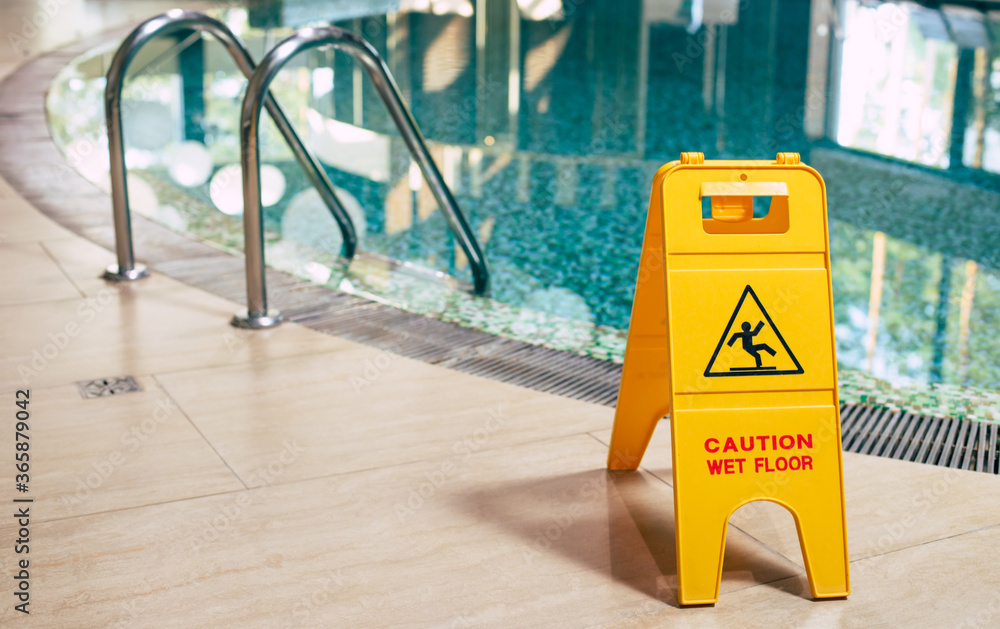 Yellow sign of wet floor plate is near the swimming pool.