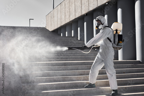 cleaning, disinfection of the city. professional worker man in white protective suit cleans the stairs with spray, sanitation and disinfection service