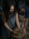 Soft focus on couple helping each other molding pottery on the machine together in dark tone.