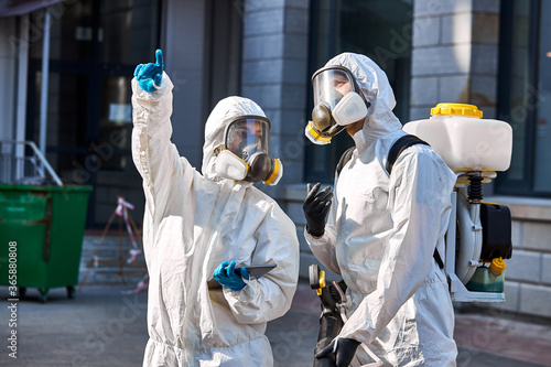 professional specialized fearless team in white protective suits and masks ready to work, clean streets of big city. two friendly workers discuss dangerous areas for cleaning