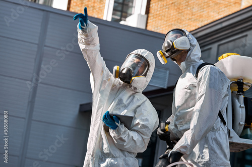 professional disinfectors looking for potentially dangerous places in city streets, sanitation service in protective suit ready to kill bacterias and infection