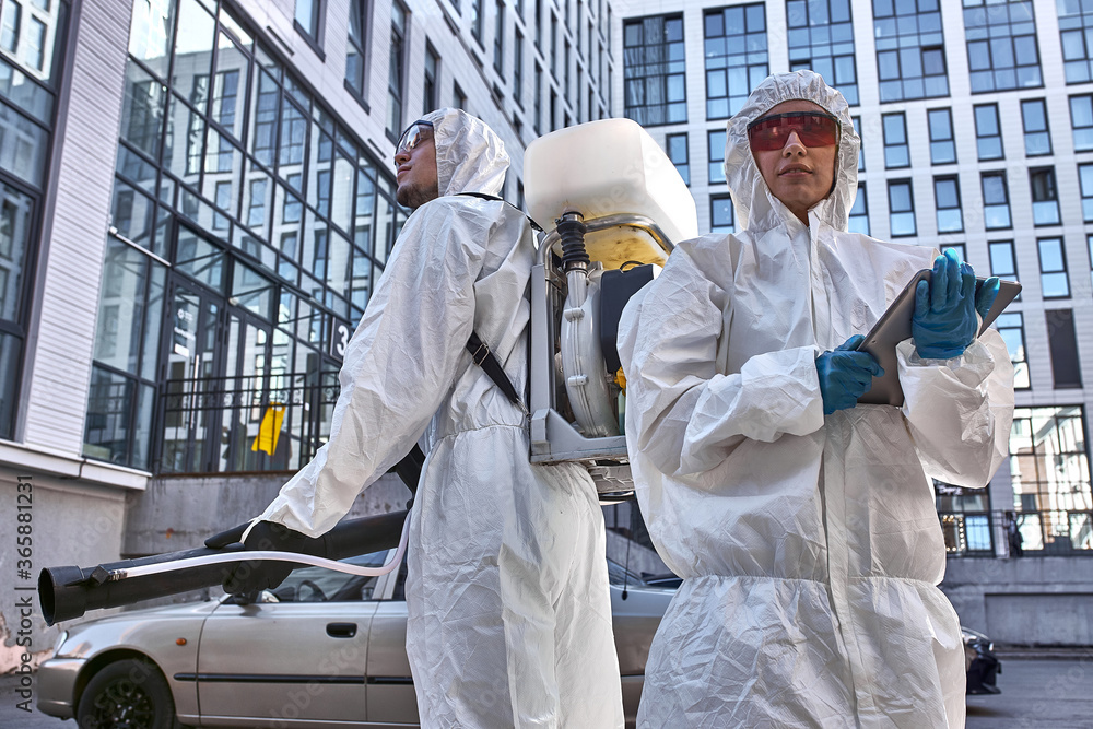 two professional disinfectors with disinfectant in the streets. professional workers in white protective wearing and gloves clean the area