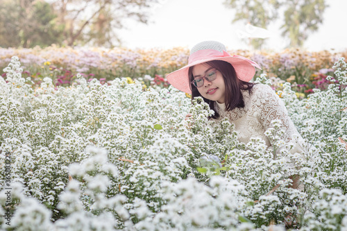 Portrait image of an asian woman with wearing pink hat smell flowers in a beautiful White cutter flower garden. © Axl4Real