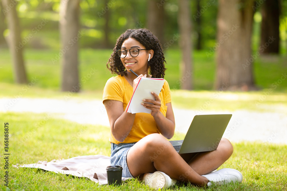 Online education. Happy black girl taking notes while watching web lesson on laptop at park Online education. Happy black girl taking notes while watching web lesson on laptop at park
