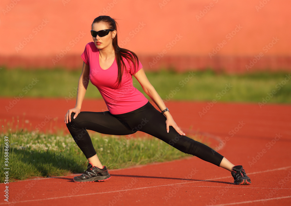 Beautiful young brunette girl warming up on the athletism track