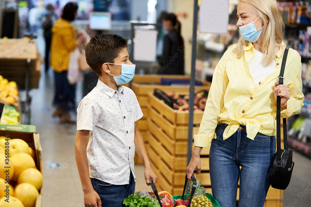mother and son choose fresh fruits and vegetables in supermarket, they are in medical protective masks, during quarantine coronavirus, covid-19
