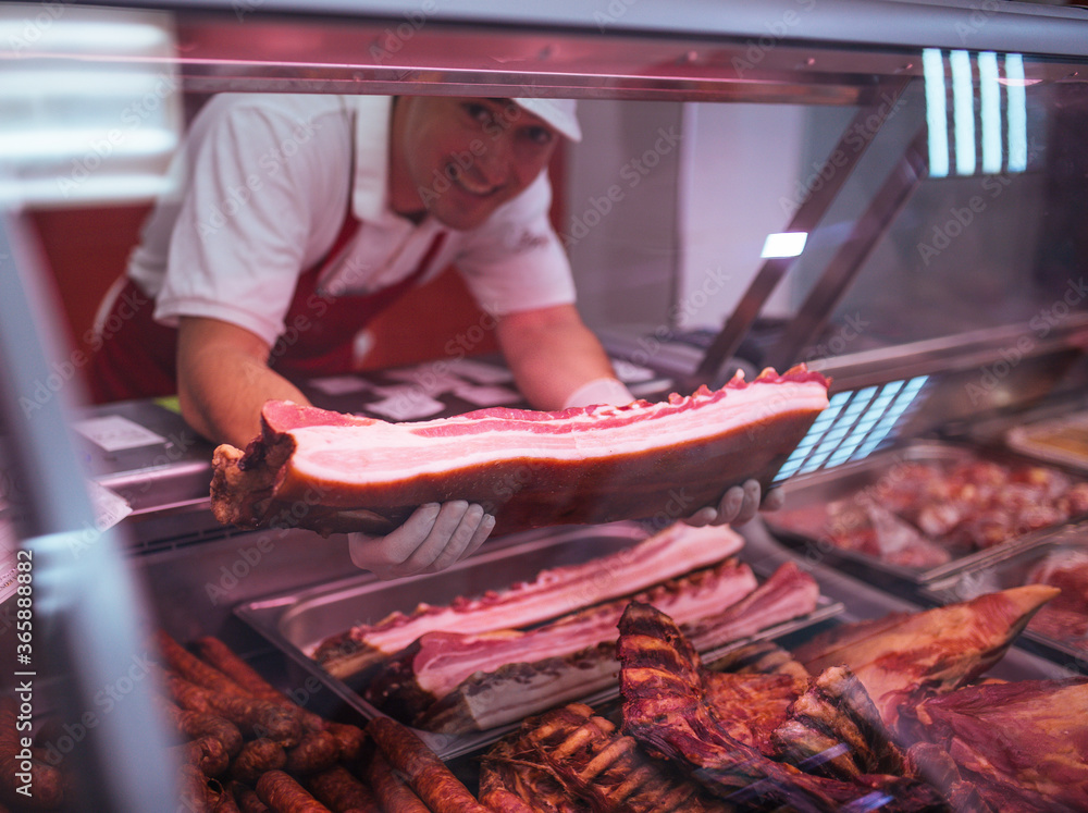 the butcher with gloves shows the customer a variety of fresh and smoked meats.Meat in focus