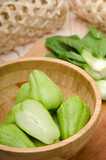 Green chayote  with background vegetables, in a wooden bowl