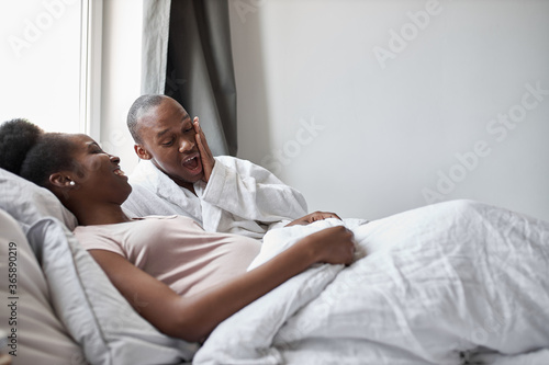 surprised african young man looking at his beutiful pregnant wife lying on bed. he is shocked by the size of his stomach