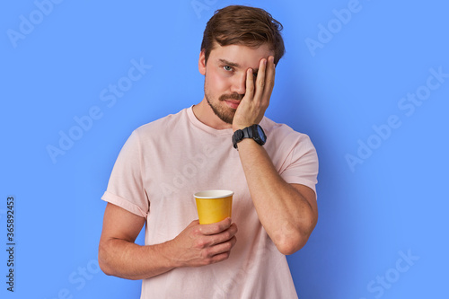 tired guy with cup of coffee, he tries to wake up, freshen up with coffee. isolated blue background