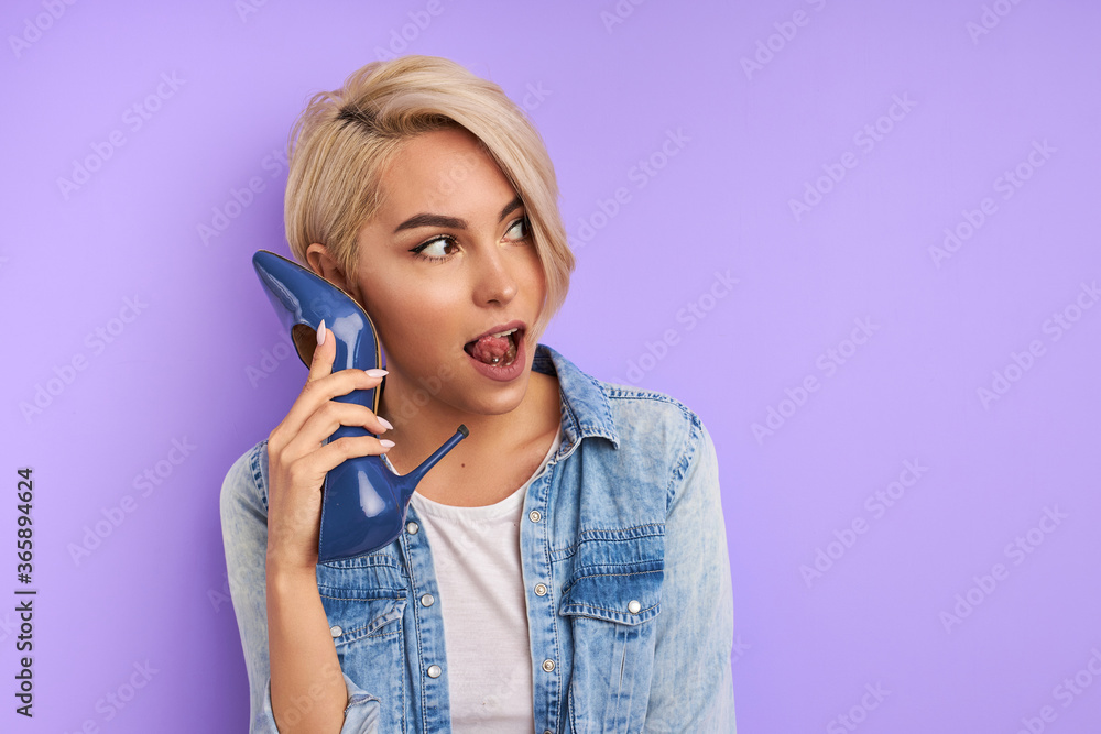 cute adorable woman hold blue shoes as phone, talk on phone. crazy funny woman is looking away isolated over purple background cute adorable woman hold blue shoes as phone, talk on phone. crazy funny woman is looking away isolated over purple background