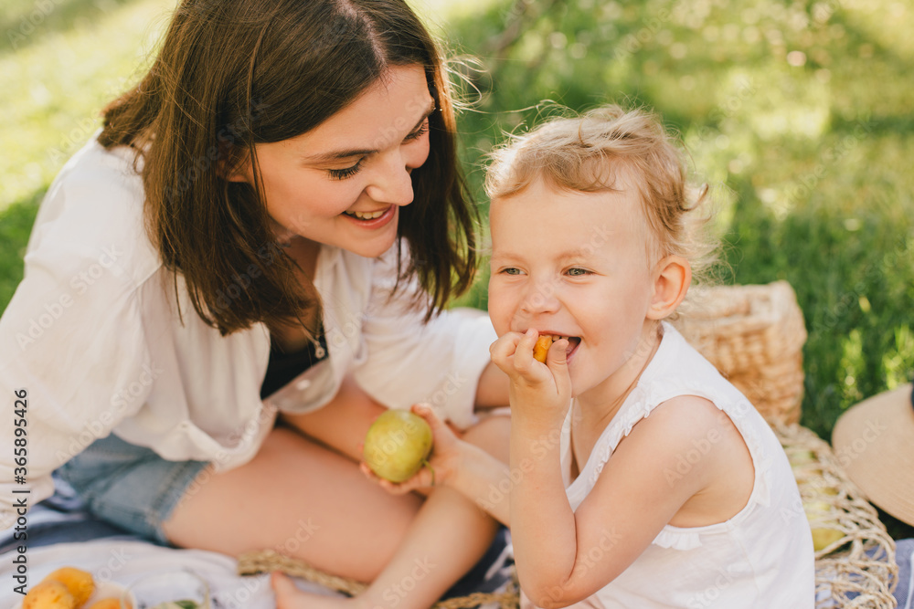Young mother and her child having cozy summer picnic with fresh lemonade and fruits in a park. Young mother and her child having cozy summer picnic with fresh lemonade and fruits in a park.