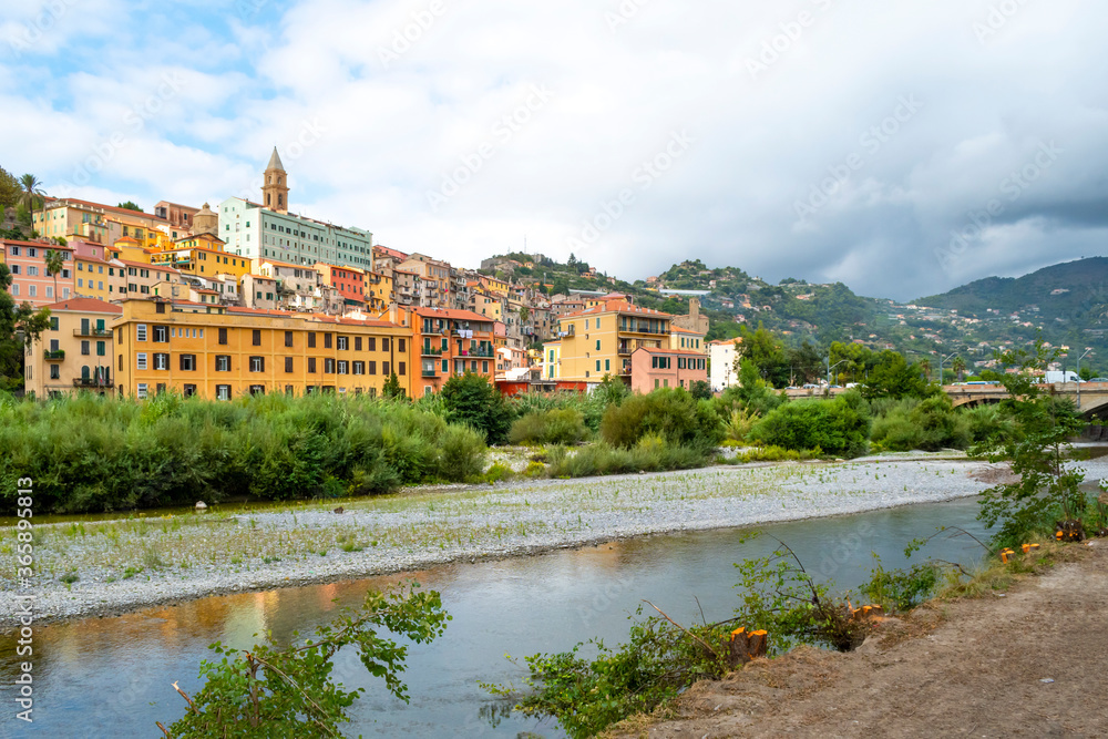 View from a riverbank across the river Roya of the village of Ventimiglia, Italy, and inland to the mountains of the Imperia region.