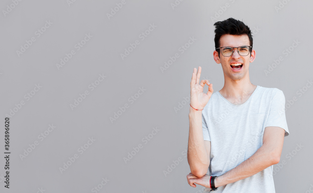 Portrait of a cheerful young man showing okay gesture isolated on the gray background Portrait of a cheerful young man showing okay gesture isolated on the gray background