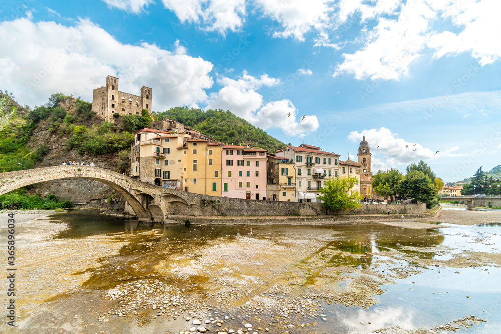 View across the Nevia River of the Saint Anthony Church, arched bridge and the medieval Castle fortress overlooking the Ligurian city of Dolceacqua, Italy,
