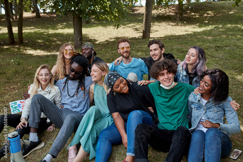 portrait of friendly happy youth on grass in the park, multiethnic group of people happy together, share funny stories and hug