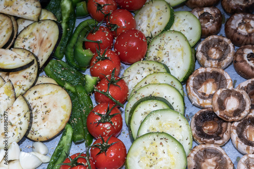 Mix of vegetables on baking paper for grilling. On the plate are tomatoes, eggplant, zucchini, peppers, garlic and mushrooms sprinkled with basil and salt.
