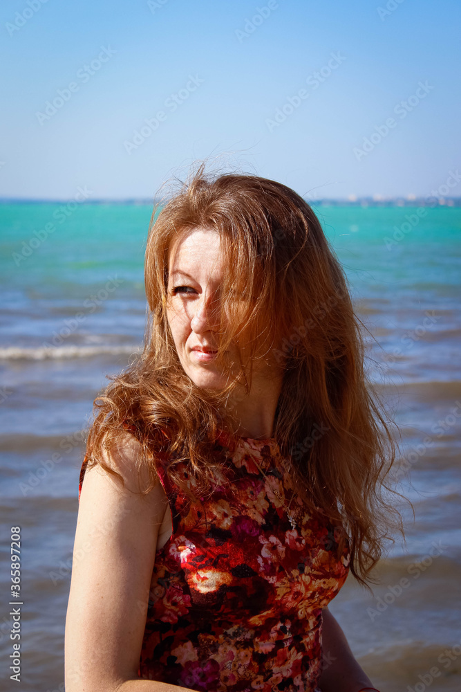 A serious young woman on the beach with gorgeous red hair and freckles.