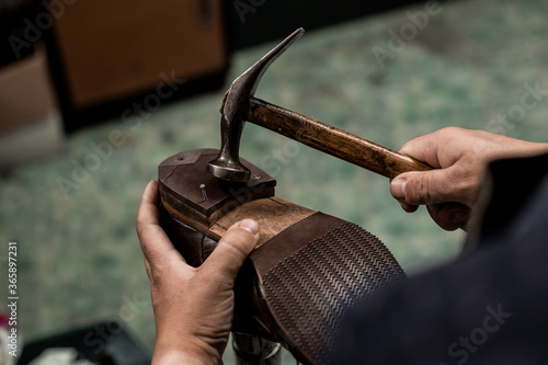 Male cobbler holding shoe and nailing a heel with hummer. Close-up on hands of professional shoemaker.