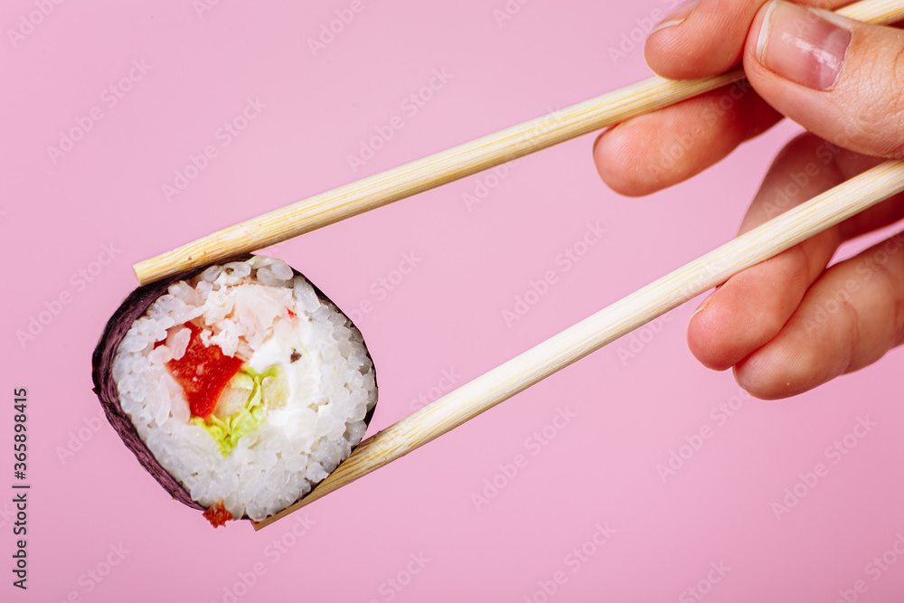 Tasty sushi roll maki with wooden chopsticks on pink background close up. Place for caption and text Tasty sushi roll maki with wooden chopsticks on pink background close up. Place for caption and text