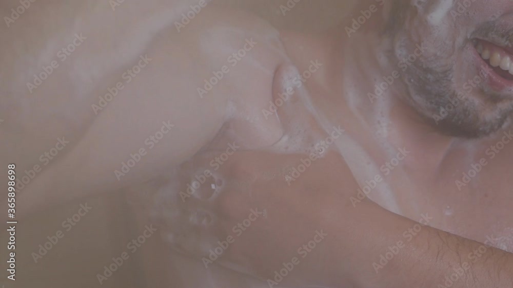 A man washes his armpits in the shower and is uncomfortable due to irritation of the armpits after shaving, he stands soaped, in the shower, under running water A man washes his armpits in the shower and is uncomfortable due to irritation of the armpits after shaving, he stands soaped, in the shower, under running water