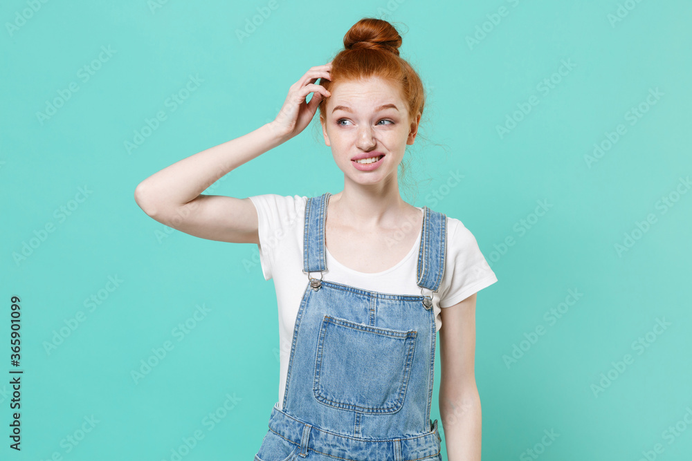 Preoccupied young readhead girl in casual denim clothes posing isolated on blue turquoise background studio portrait. People lifestyle concept. Mock up copy space. Put hand on head, looking aside. Preoccupied young readhead girl in casual denim clothes posing isolated on blue turquoise background studio portrait. People lifestyle concept. Mock up copy space. Put hand on head, looking aside.