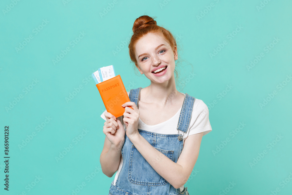 Cheerful young readhead girl in casual denim clothes isolated on blue turquoise background. Passenger traveling abroad to travel on weekends getaway. Air flight journey concept. Hold passport tickets. Cheerful young readhead girl in casual denim clothes isolated on blue turquoise background. Passenger traveling abroad to travel on weekends getaway. Air flight journey concept. Hold passport tickets.