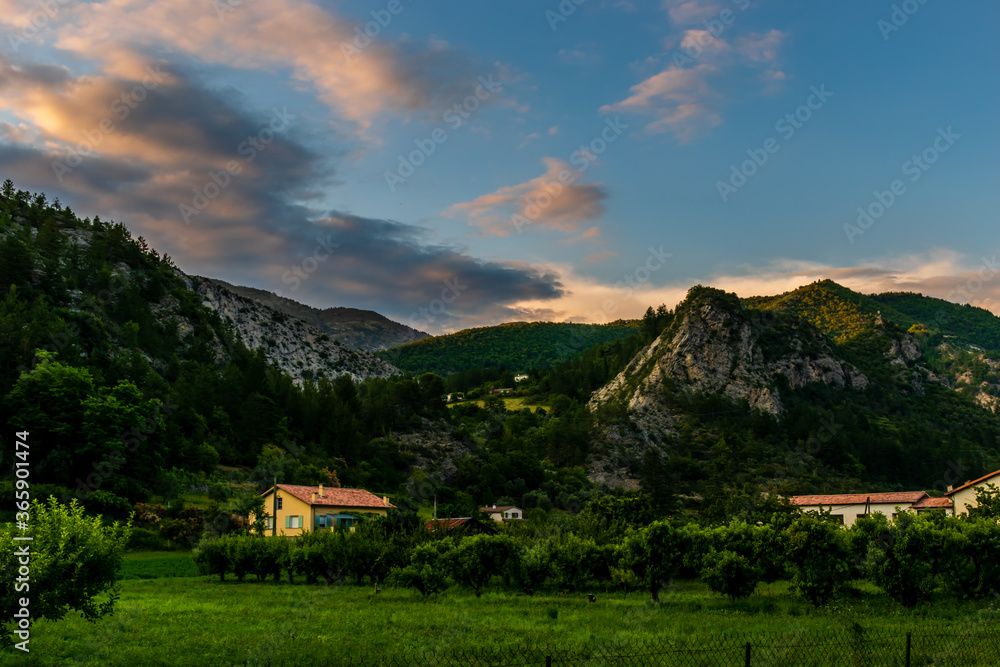 A picturesque landscape view of houses and fields in a valley in the Alps mountains after sunset (Puget-Theniers, Alpes-Maritimes, France)
