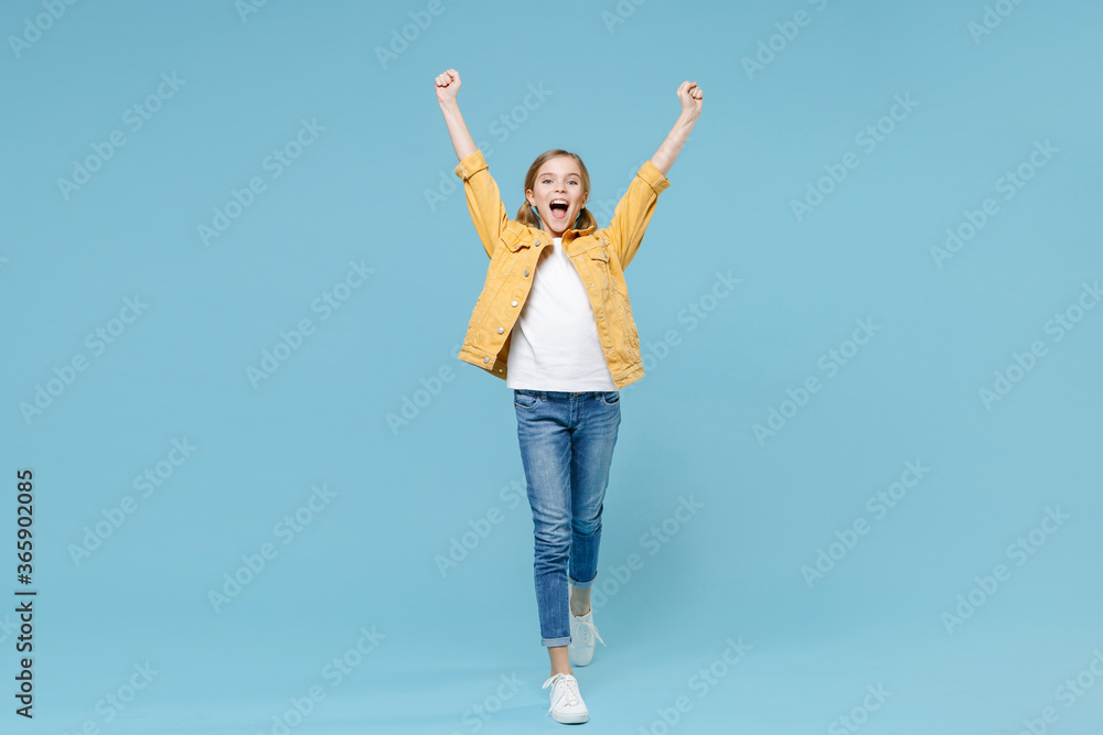 Full length portrait of excited little blonde kid girl 12-13 years old in yellow jacket isolated on blue wall background. Childhood lifestyle concept. Mock up copy space. Clenching fists like winner. Full length portrait of excited little blonde kid girl 12-13 years old in yellow jacket isolated on blue wall background. Childhood lifestyle concept. Mock up copy space. Clenching fists like winner.
