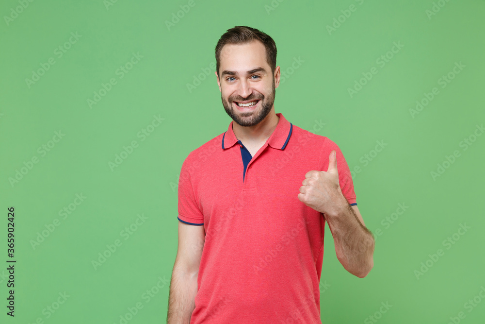 Smiling young bearded man guy in casual red pink t-shirt posing isolated on green wall background studio portrait. People sincere emotions lifestyle concept. Mock up copy space. Showing thumb up. Smiling young bearded man guy in casual red pink t-shirt posing isolated on green wall background studio portrait. People sincere emotions lifestyle concept. Mock up copy space. Showing thumb up.