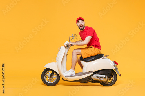 Delivery man in red cap t-shirt uniform driving moped motorbike scooter isolated on yellow background studio Guy employee working courier Service quarantine pandemic coronavirus virus covid-19 concept © ViDi Studio