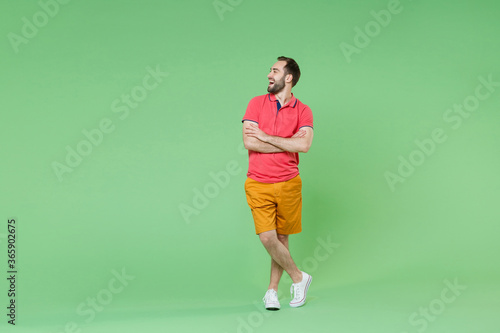 Funny young bearded man guy in casual red pink t-shirt posing isolated on green background studio portrait. People emotions lifestyle concept. Mock up copy space. Holding hands crossed, looking aside. © ViDi Studio