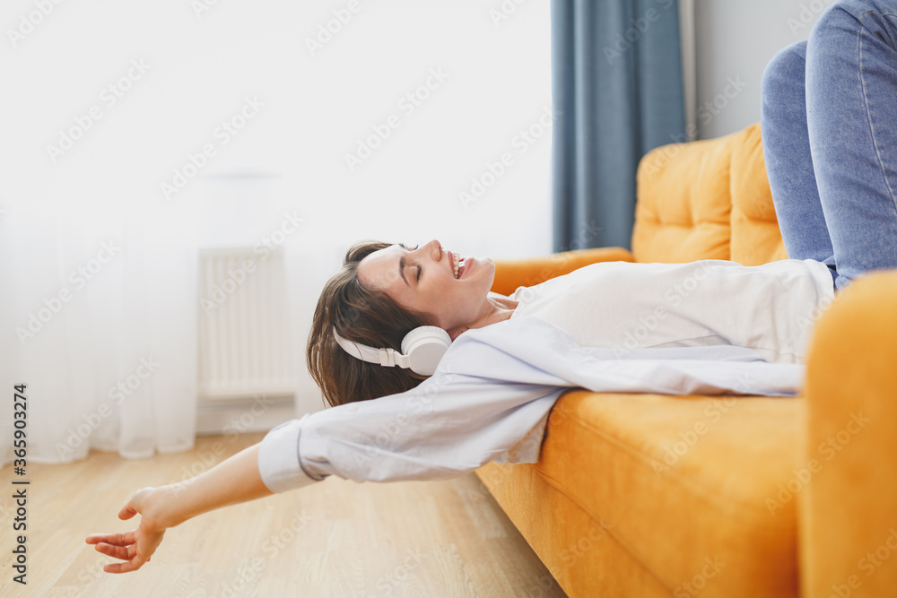 Funny young woman girl in casual clothes lying on couch spending time in living room at home. Rest relax good mood leisure lifestyle concept. Mock up copy space. Listen music with headphones dancing. Funny young woman girl in casual clothes lying on couch spending time in living room at home. Rest relax good mood leisure lifestyle concept. Mock up copy space. Listen music with headphones dancing.