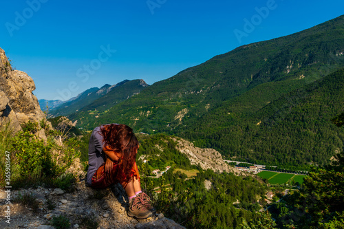 A full body shot of a tired young Caucasian redhead hiker sitting on a boulder on a hiking path in the French Alps during sunset © k.dei