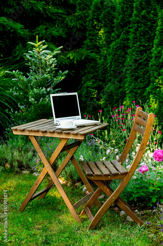 Cup of tea and laptop computer on a wooden table in a garden