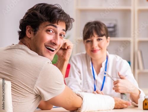 Young man with bandaged arm visiting female doctor traumatologis