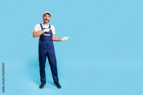 Full length surprised handyman in uniform pointing at copy space, advertising area for idea presentation, looking shocked at camera. Profession of service industry, builder or contractor. isolated