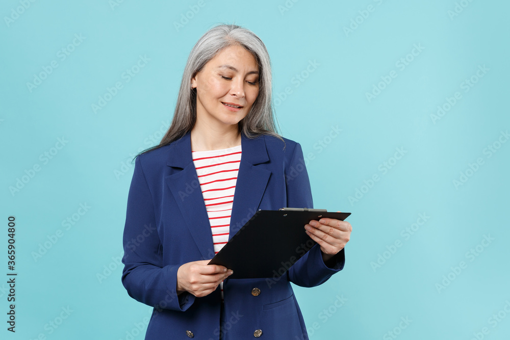 Beautiful gray-haired business woman in blue suit isolated on blue wall background studio portrait. Achievement career wealth business concept. Mock up copy space. Hold clipboard with papers document. Beautiful gray-haired business woman in blue suit isolated on blue wall background studio portrait. Achievement career wealth business concept. Mock up copy space. Hold clipboard with papers document.