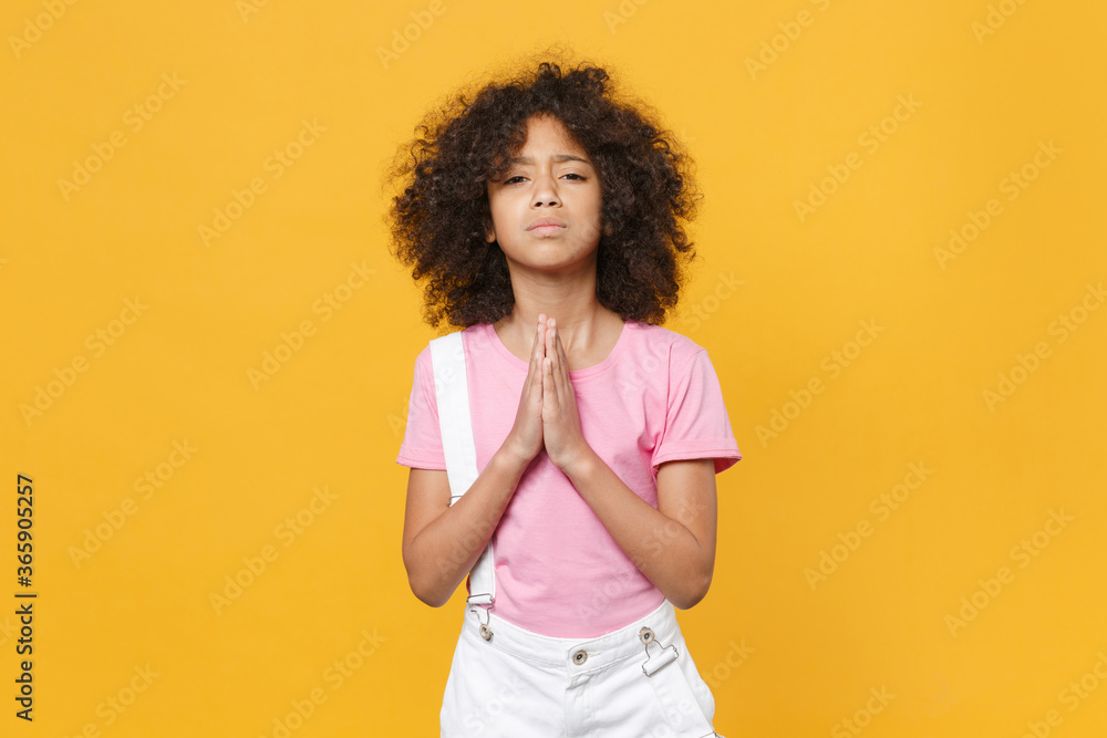 Pleading little african american kid girl 12-13 years old in pink t-shirt isolated on yellow background studio portrait. Childhood lifestyle concept. Mock up copy space. Hold hands folded in prayer. Pleading little african american kid girl 12-13 years old in pink t-shirt isolated on yellow background studio portrait. Childhood lifestyle concept. Mock up copy space. Hold hands folded in prayer.